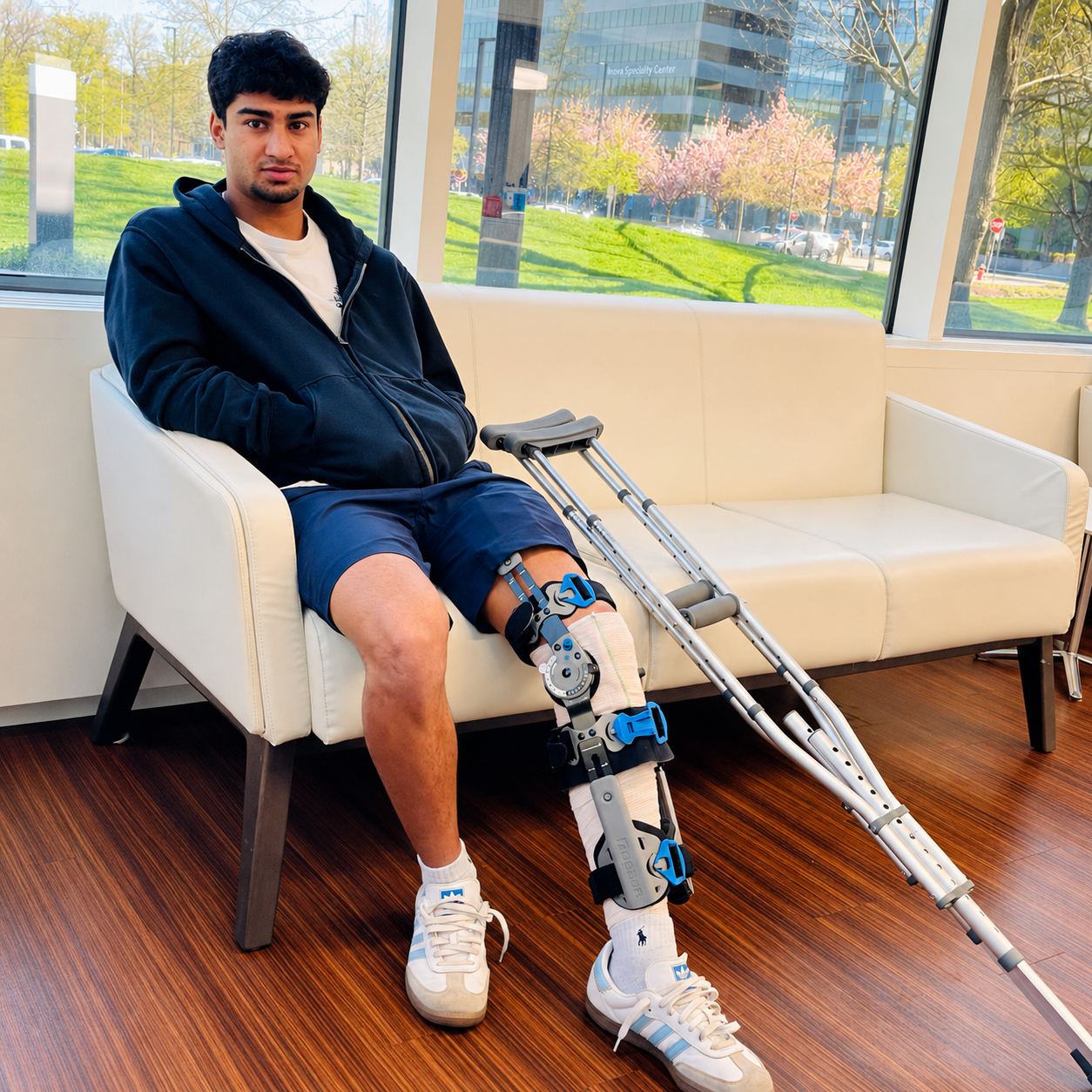 Young man recovering after ACL reconstruction surgery, seated with a leg brace and crutches in a sunlit hospital waiting area.